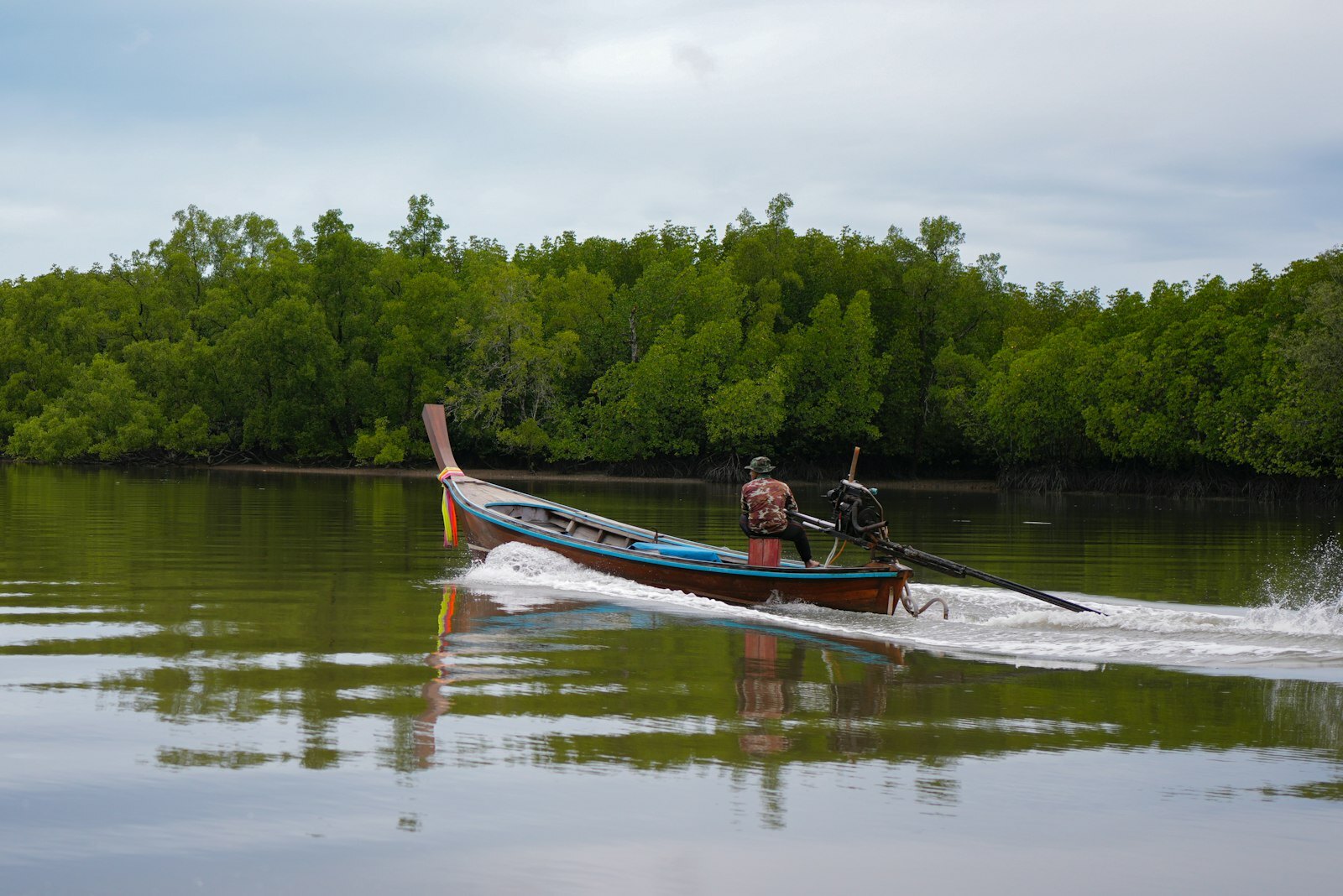 A person steers a longtail boat through calm water.